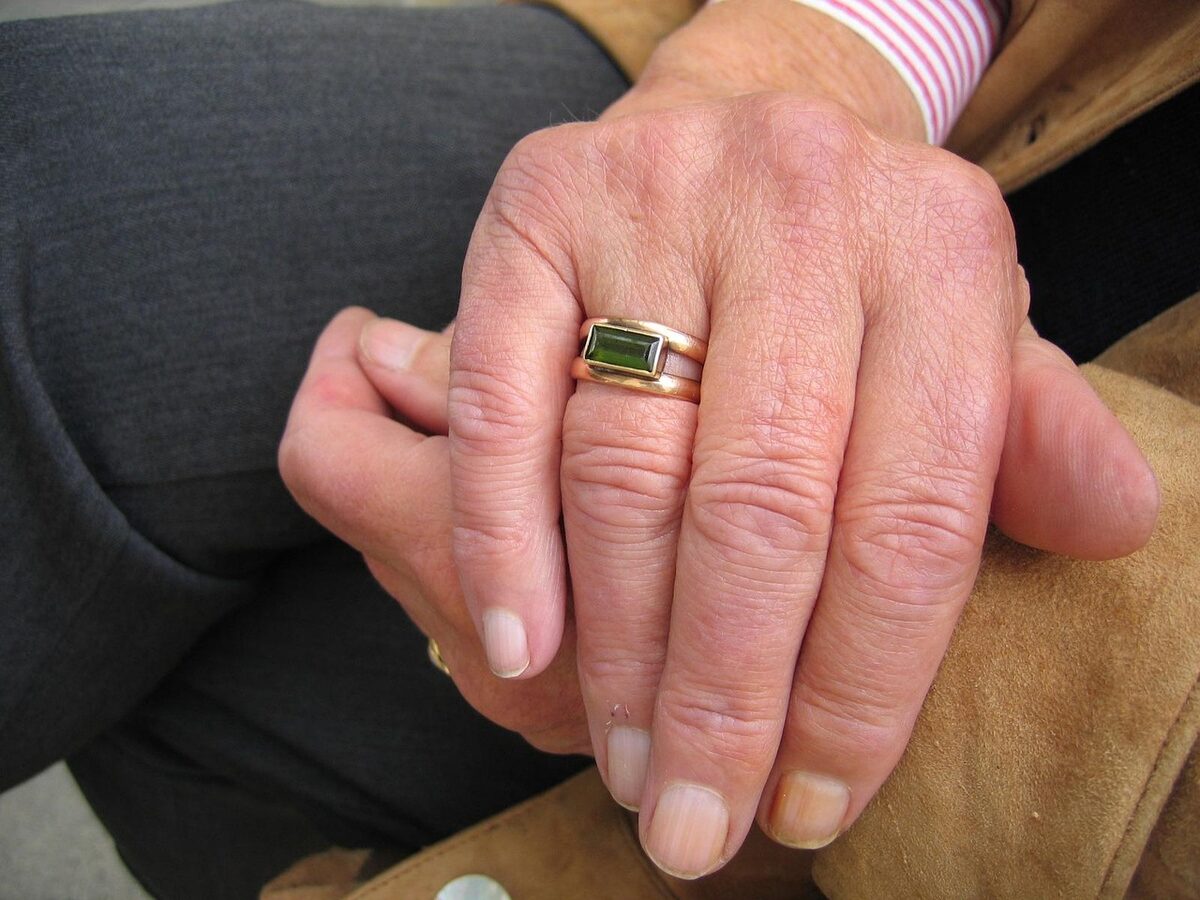 Close-up of an elderly person's clasped hands resting in their lap.