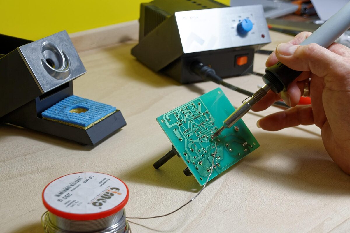 Engineer hand-soldering a component onto a circuit board at a soldering station.