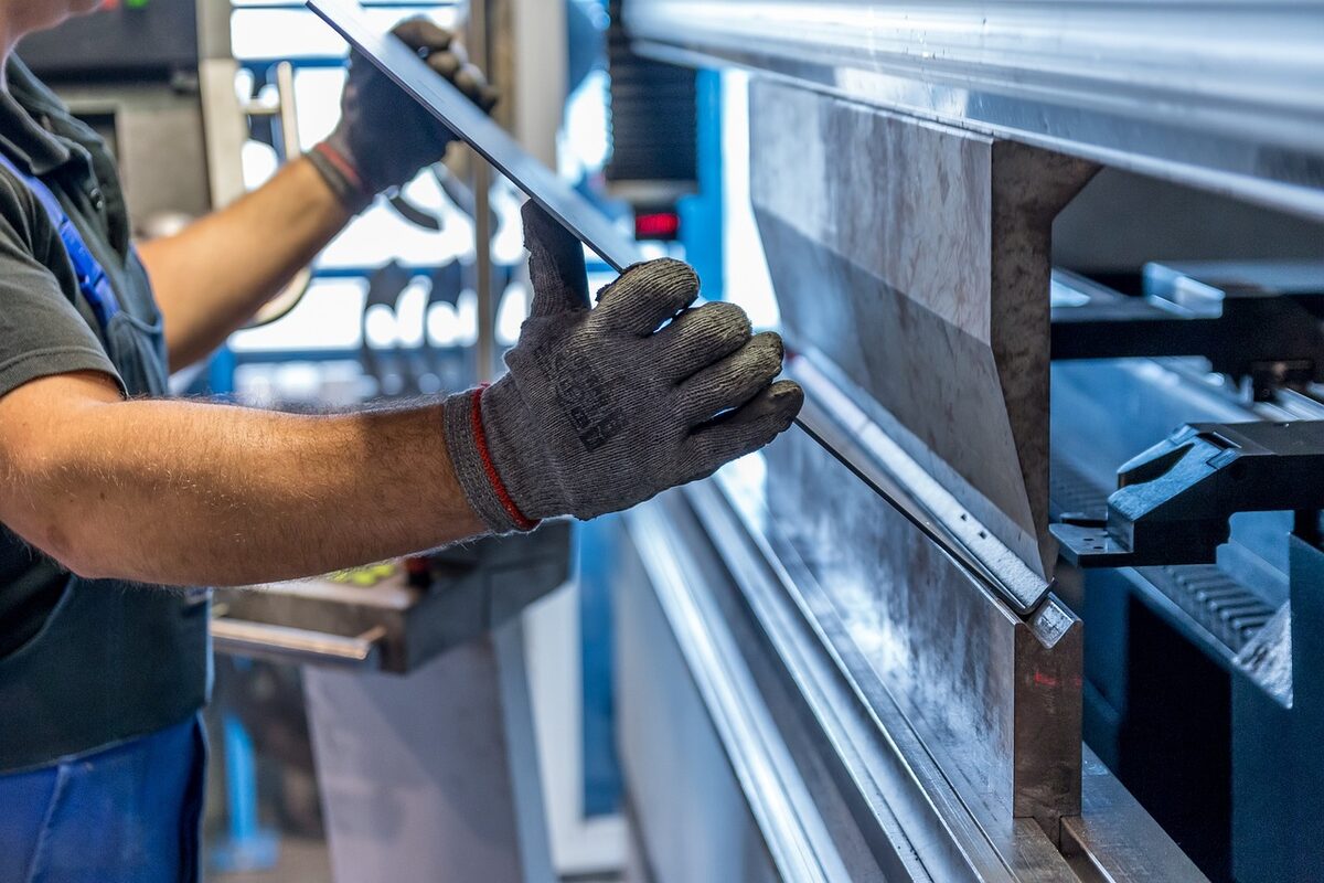 Worker's gloved hands feeding a metal sheet into an industrial press brake.