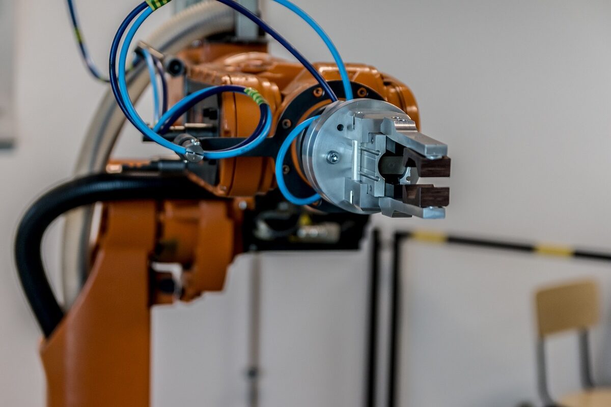 Close-up of an orange industrial robot arm with a metal gripper and pneumatic hoses.