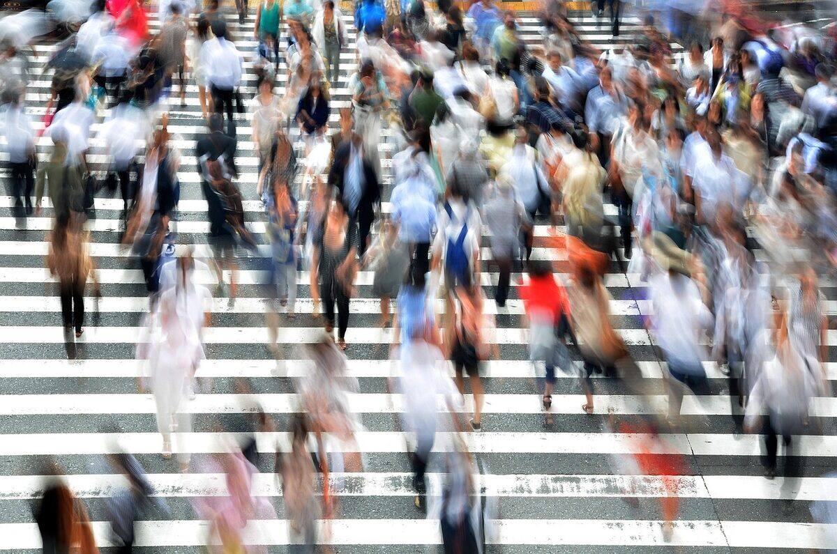 Motion-blurred crowd of pedestrians crossing a striped crosswalk.